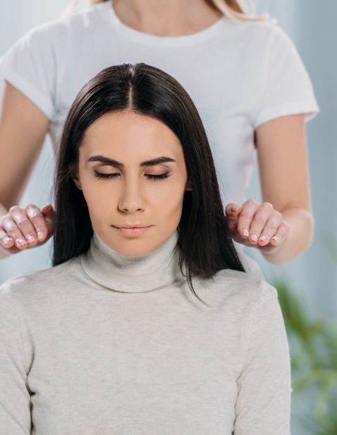 cropped shot of female healer doing reiki healing therapy session to young woman with closed eyes
